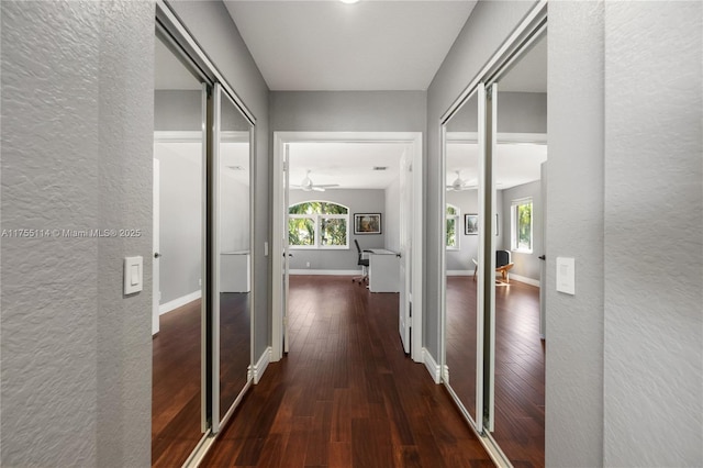 hall featuring baseboards, wood-type flooring, and a textured wall