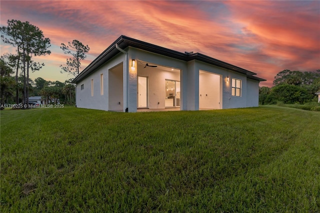 back of property with stucco siding, a ceiling fan, and a yard