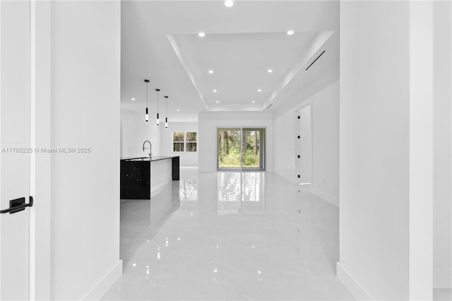 unfurnished living room with a tray ceiling, recessed lighting, marble finish floor, and baseboards