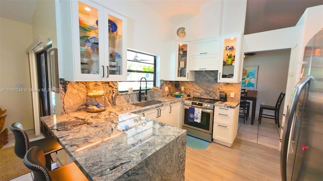 kitchen featuring light stone countertops, a peninsula, a sink, stainless steel appliances, and tasteful backsplash