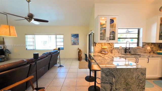 kitchen with light tile patterned floors, light stone countertops, a sink, white cabinets, and tasteful backsplash