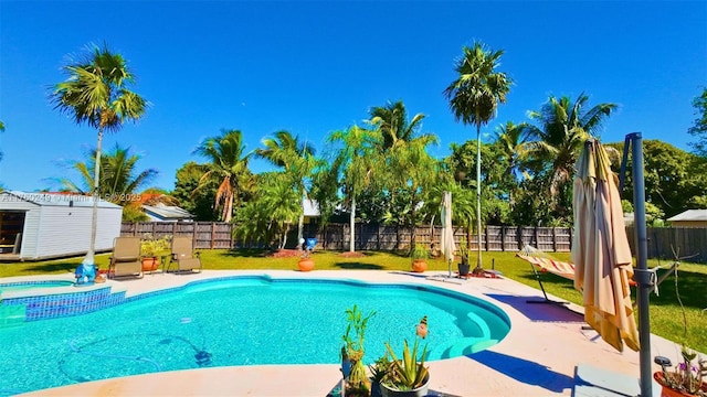 view of pool featuring a fenced backyard, a pool with connected hot tub, an outdoor structure, a storage unit, and a patio area