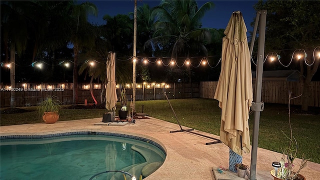 pool at night featuring a fenced in pool, a lawn, a fenced backyard, and a patio area