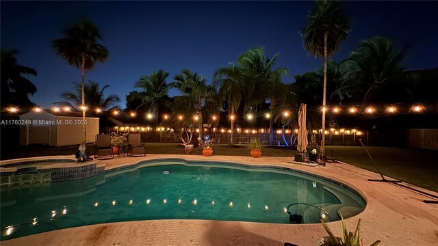 pool at night with fence, a pool with connected hot tub, and a patio area