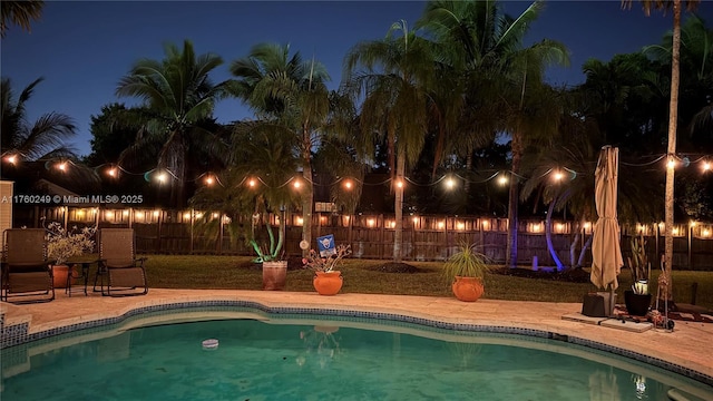 pool at twilight featuring a fenced in pool, a fenced backyard, and a patio area