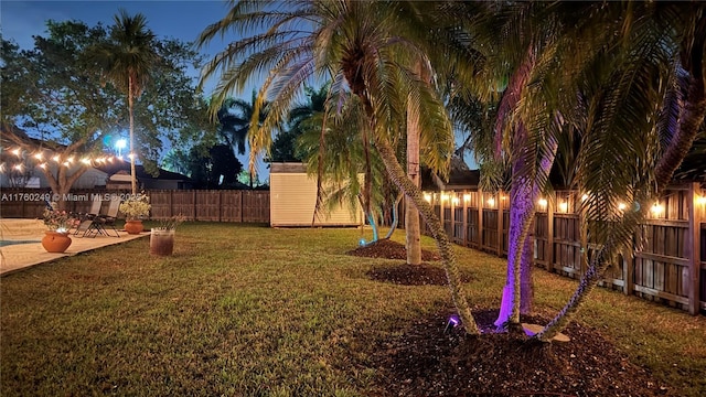 yard at night featuring a storage unit, an outbuilding, a fenced backyard, and a patio area