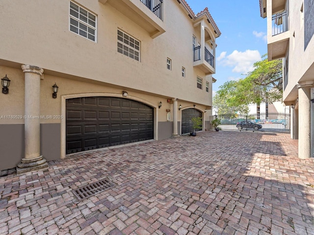 view of side of property with stucco siding, decorative driveway, a garage, and fence