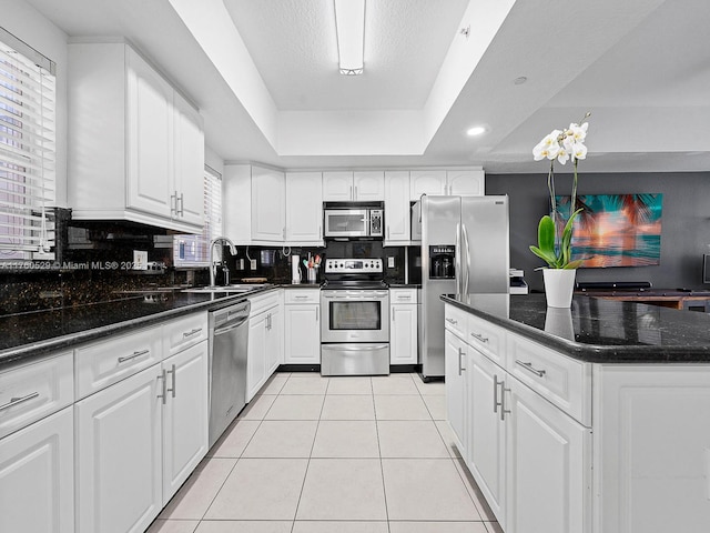 kitchen with a sink, stainless steel appliances, light tile patterned floors, decorative backsplash, and a raised ceiling