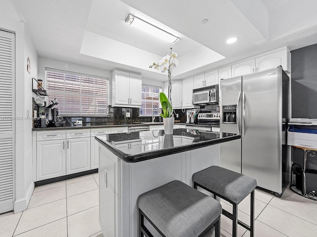 kitchen with a tray ceiling, stainless steel appliances, tasteful backsplash, and light tile patterned floors