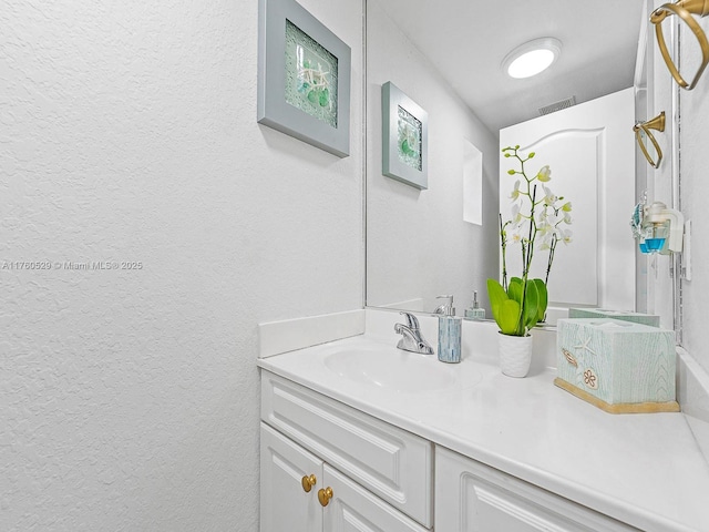 bathroom featuring vanity, a textured wall, and visible vents