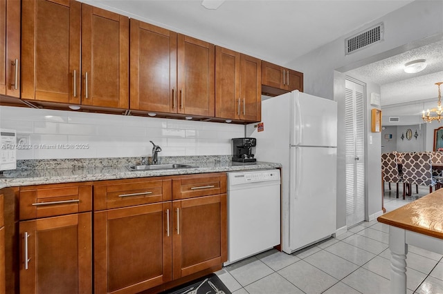 kitchen with white appliances, light tile patterned floors, brown cabinetry, visible vents, and a sink