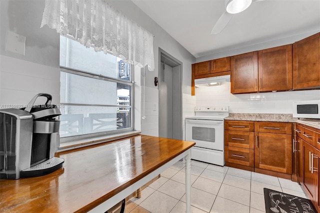 kitchen featuring white appliances, light tile patterned floors, brown cabinetry, and under cabinet range hood