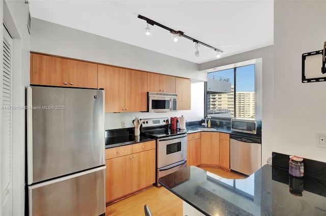 kitchen with dark stone counters, appliances with stainless steel finishes, a peninsula, light wood-style floors, and a sink