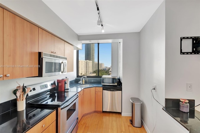 kitchen with light wood finished floors, dark countertops, rail lighting, stainless steel appliances, and a sink