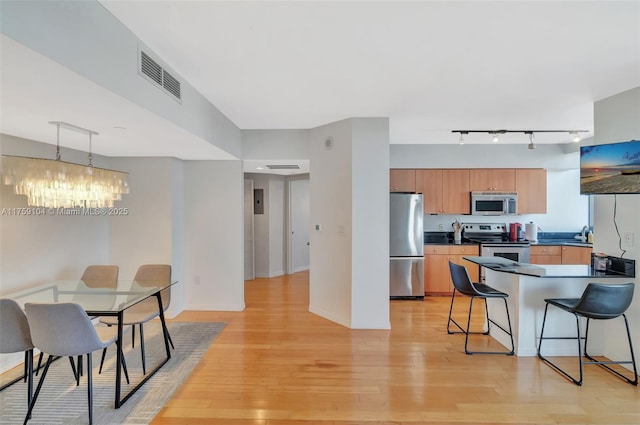 kitchen featuring light wood-type flooring, stainless steel appliances, dark countertops, and visible vents