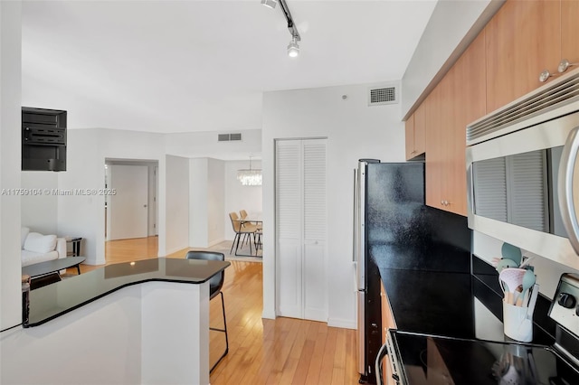 kitchen featuring visible vents, light wood-style flooring, stainless steel microwave, dark countertops, and electric range oven