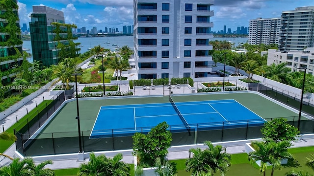 view of tennis court with a view of city, fence, and a water view