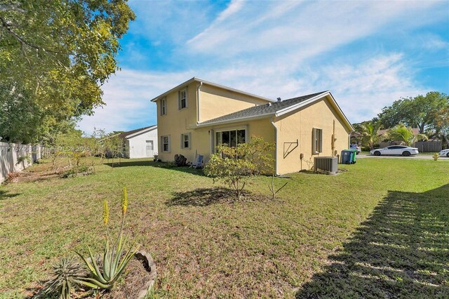 rear view of property with cooling unit, fence, a lawn, and stucco siding