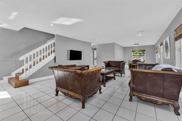 living room featuring light tile patterned floors, baseboards, a textured ceiling, and stairs