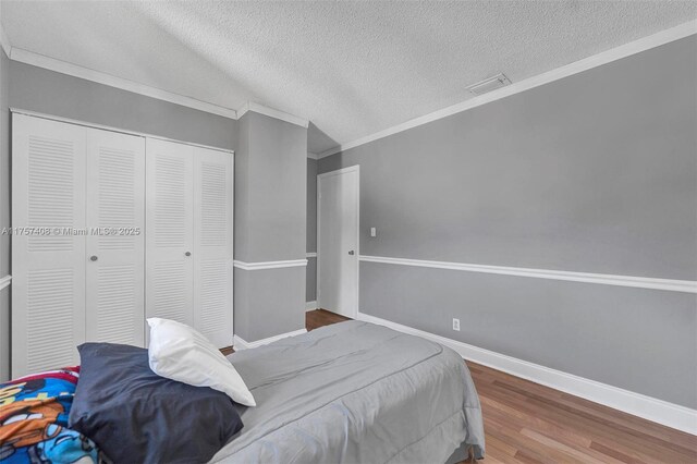 bedroom featuring visible vents, baseboards, ornamental molding, wood finished floors, and a textured ceiling