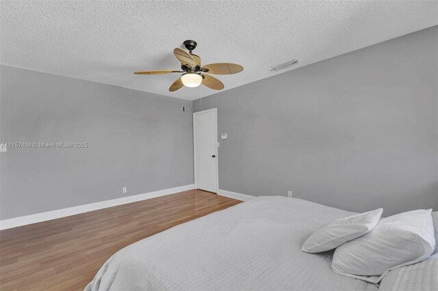 bedroom featuring a ceiling fan, visible vents, wood finished floors, baseboards, and a textured ceiling