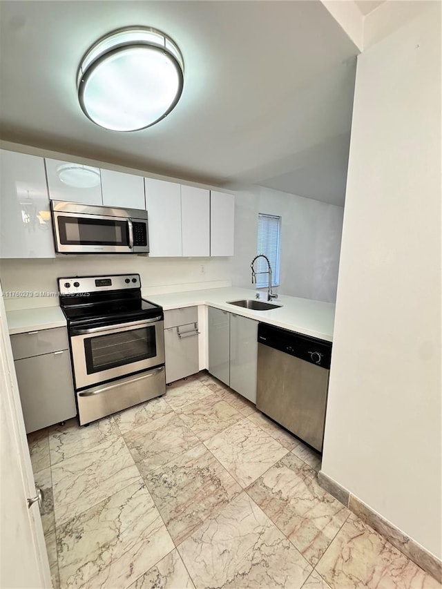 kitchen featuring marble finish floor, stainless steel appliances, light countertops, and a sink