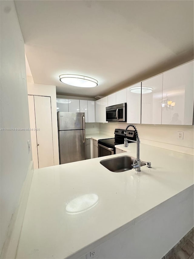 kitchen featuring a peninsula, a sink, light countertops, white cabinets, and appliances with stainless steel finishes