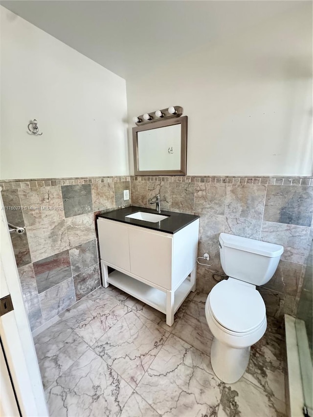 bathroom featuring vanity, a wainscoted wall, tile walls, toilet, and marble finish floor