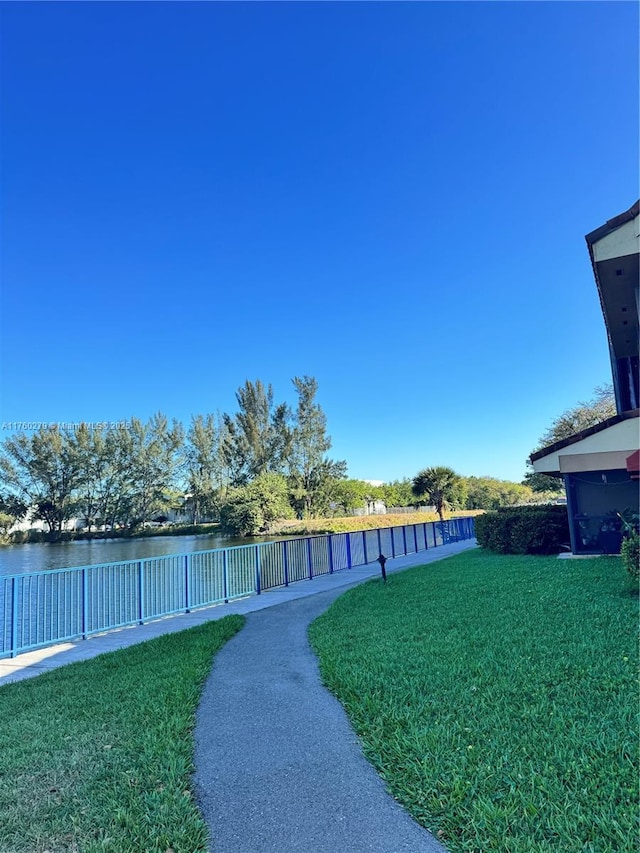 view of community featuring a water view, a lawn, and fence