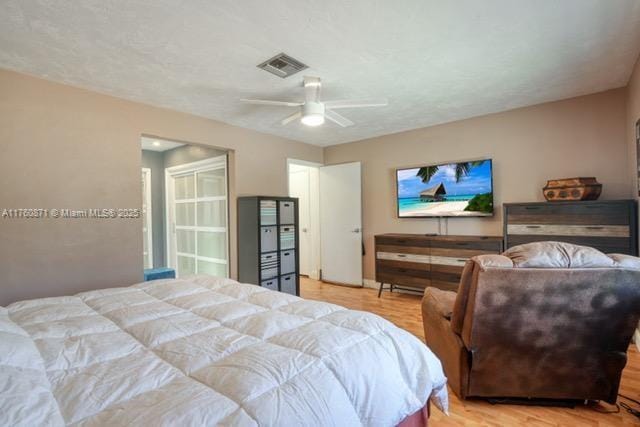 bedroom featuring a ceiling fan, wood finished floors, visible vents, and a textured ceiling