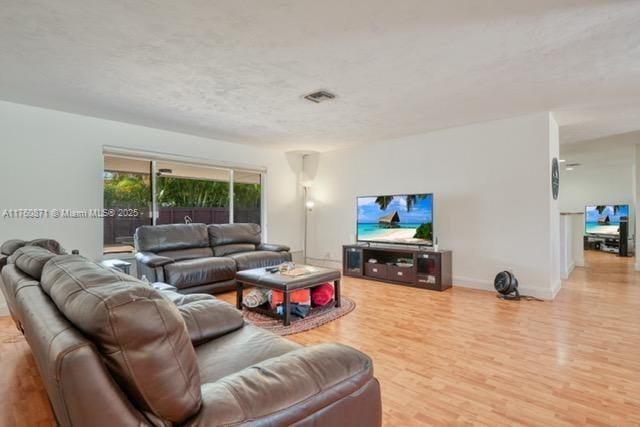 living area with baseboards, wood finished floors, visible vents, and a textured ceiling