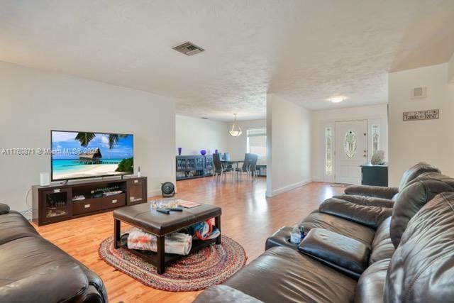 living room with a textured ceiling, light wood-style floors, visible vents, and baseboards