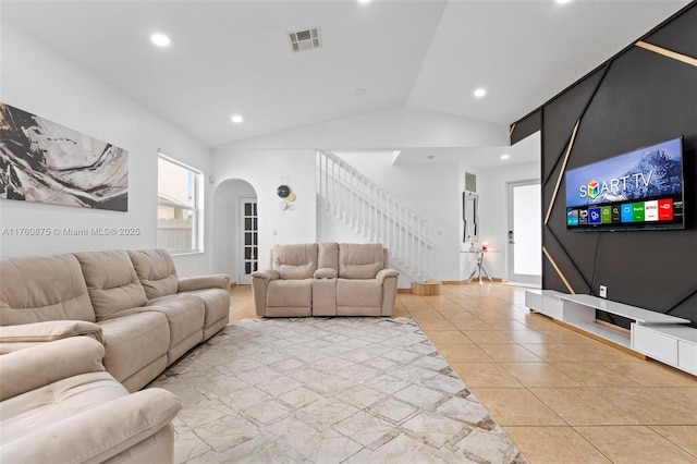 living room with light tile patterned floors, visible vents, arched walkways, stairs, and vaulted ceiling
