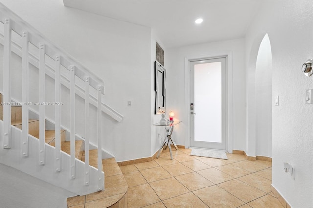 entryway with stairs, tile patterned floors, arched walkways, and baseboards