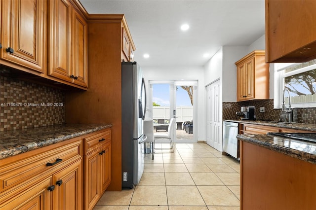 kitchen with brown cabinetry, light tile patterned floors, dark stone countertops, and appliances with stainless steel finishes