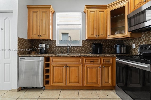 kitchen featuring a sink, dark stone countertops, appliances with stainless steel finishes, light tile patterned flooring, and decorative backsplash