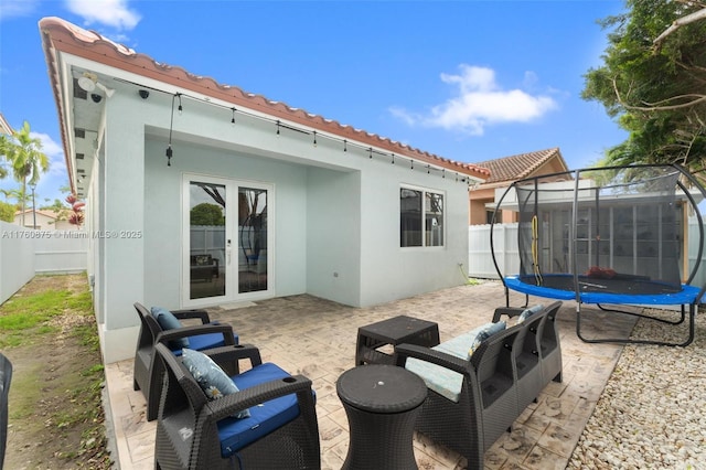rear view of house with stucco siding, a tile roof, a patio, a trampoline, and french doors
