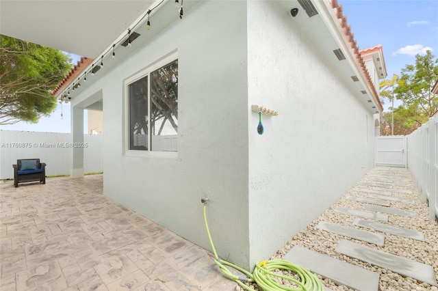view of side of property with stucco siding, a patio, a fenced backyard, and a tiled roof