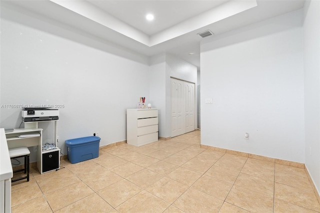 office featuring light tile patterned flooring, visible vents, baseboards, and a tray ceiling