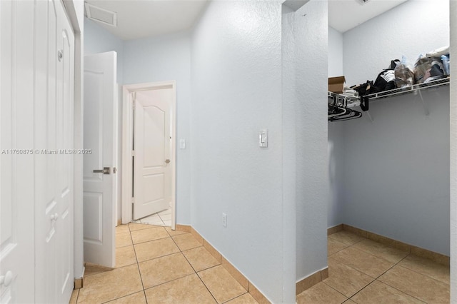 hallway with light tile patterned floors, visible vents, and baseboards