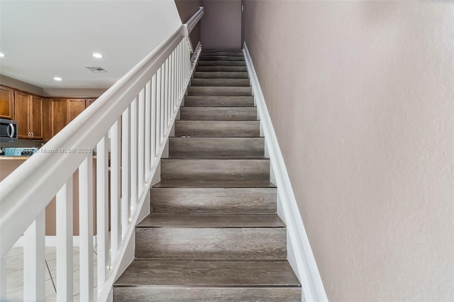 staircase with baseboards, wood finished floors, visible vents, and recessed lighting