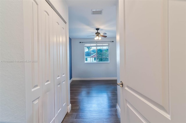hallway featuring dark wood finished floors, visible vents, and baseboards