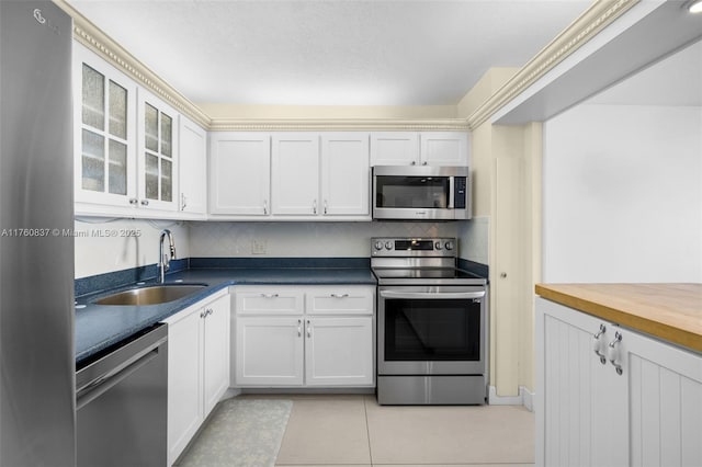 kitchen featuring a sink, backsplash, appliances with stainless steel finishes, light tile patterned floors, and glass insert cabinets