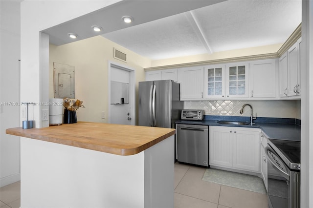 kitchen featuring a sink, wooden counters, appliances with stainless steel finishes, and light tile patterned flooring