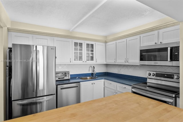 kitchen featuring backsplash, glass insert cabinets, appliances with stainless steel finishes, a textured ceiling, and a sink