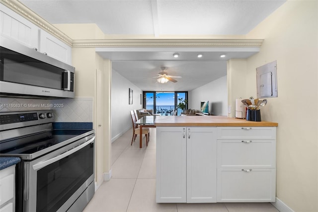 kitchen with tasteful backsplash, wooden counters, light tile patterned floors, white cabinets, and stainless steel appliances