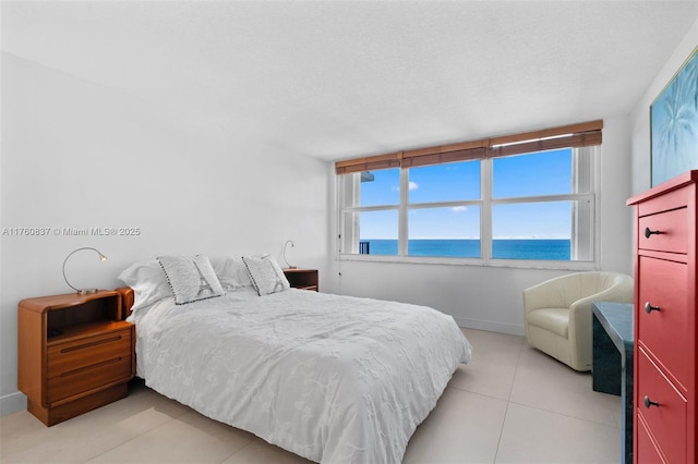 bedroom featuring light tile patterned floors, baseboards, a water view, and a textured ceiling