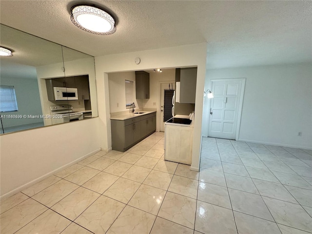 kitchen with a sink, a textured ceiling, white appliances, light tile patterned floors, and baseboards