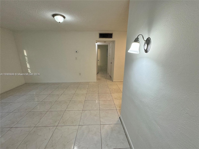 unfurnished room featuring light tile patterned floors, visible vents, baseboards, and a textured ceiling