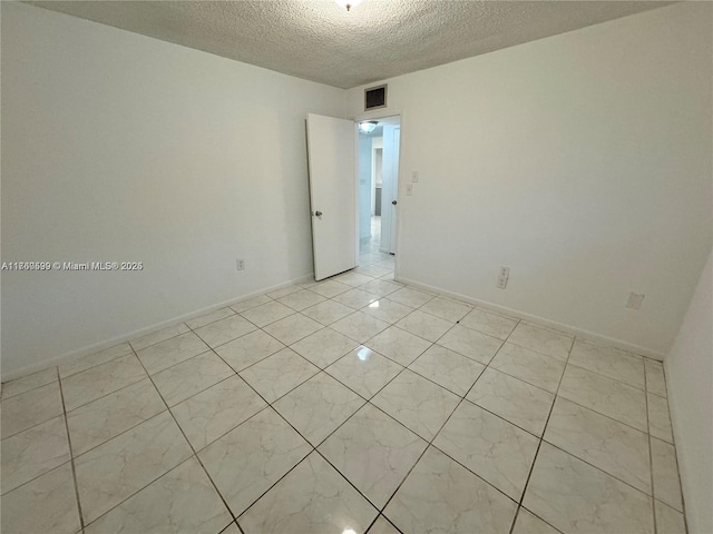 spare room featuring light tile patterned floors, visible vents, a textured ceiling, and baseboards